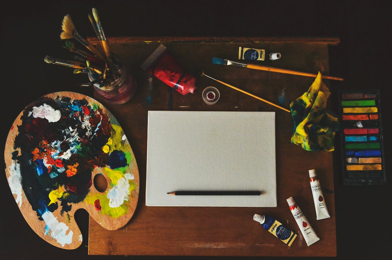 Vibrant artist workspace with paintbrushes, palette, paint tubes, and blank canvas.