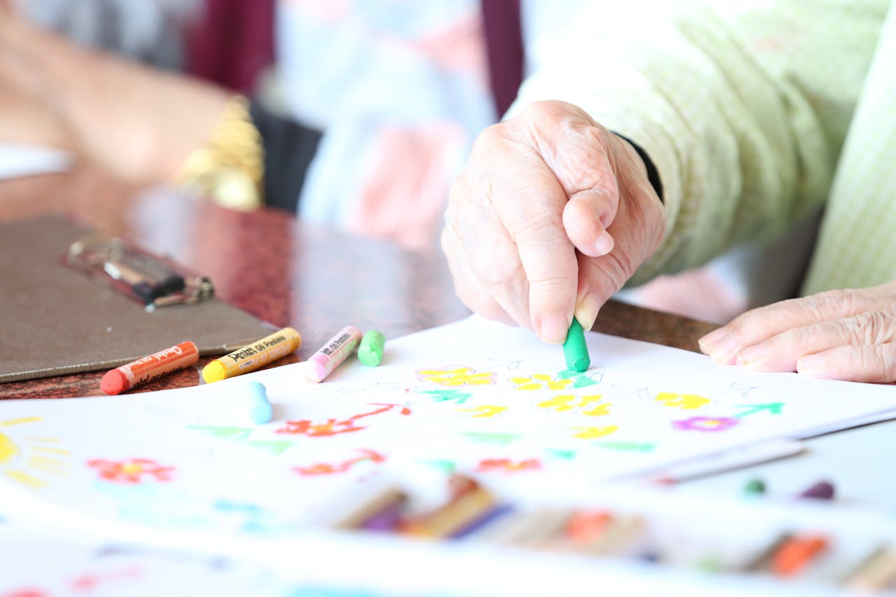 gallery-3 Close-up of a senior woman drawing with crayons in an art therapy session indoors.