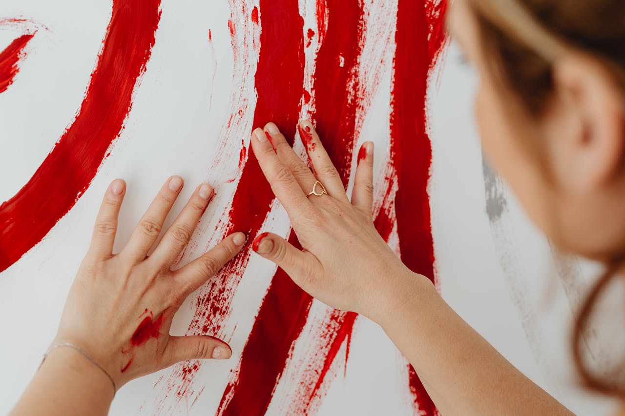 gallery-2 Close-up of a woman using her hands to paint abstract red strokes on a canvas.
