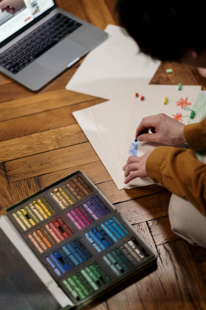 why-choose-us Adult engaged in online art class, using oil pastels on wooden floor.
